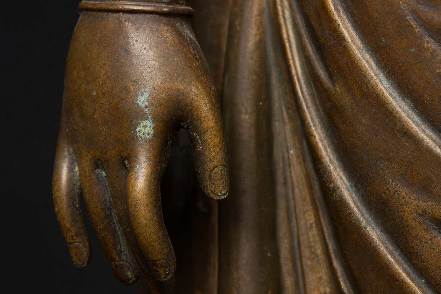 Close-up of a temple bronze showing warm brown patina, brighter raised areas, dark recesses, and small pale green deposits.