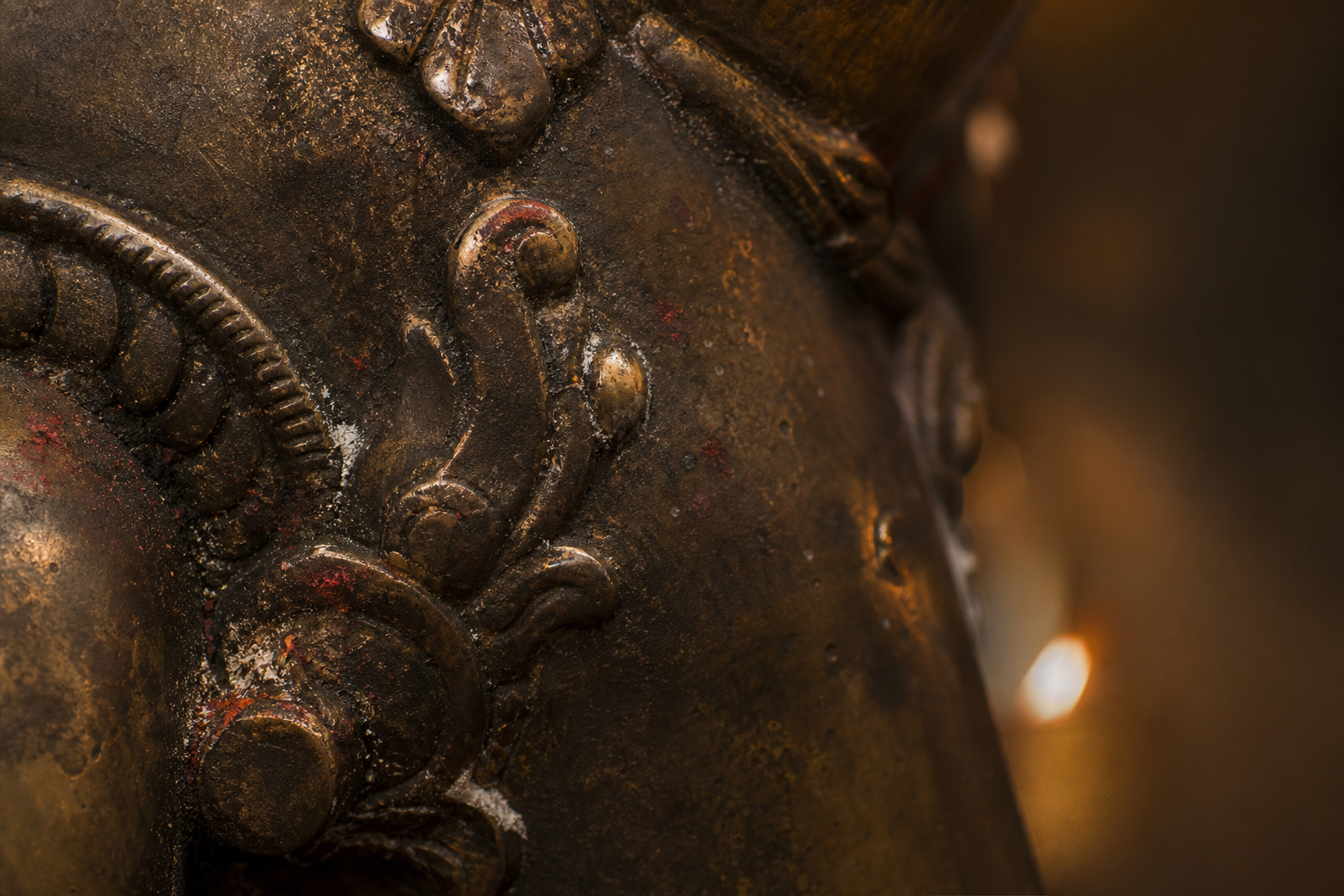 Macro view of an aged bronze ornament with dark patina in recesses, softly glowing raised ridges, and traces of ritual pigment.