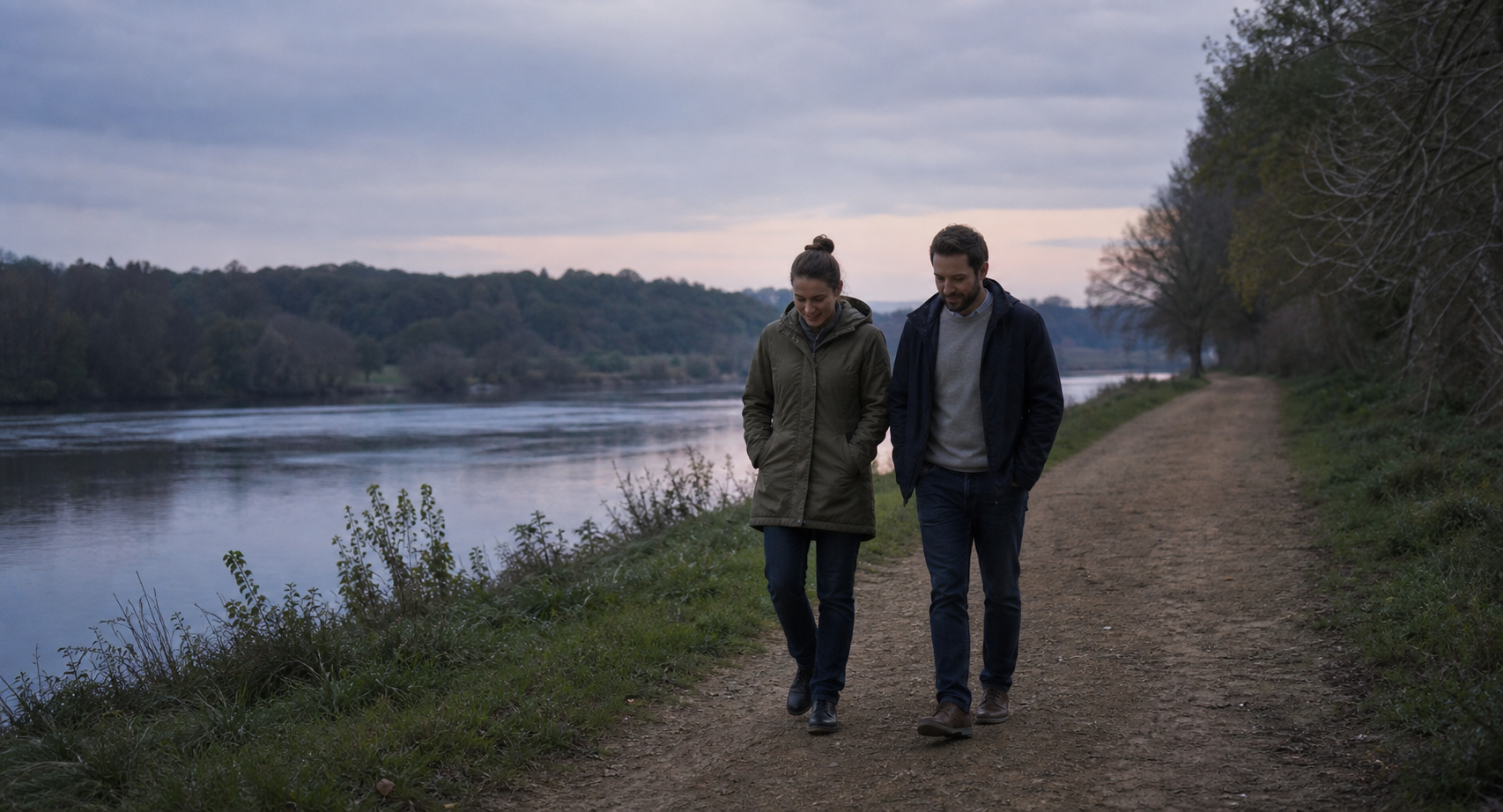 Two adults walk side by side at an even pace along a quiet riverside path.