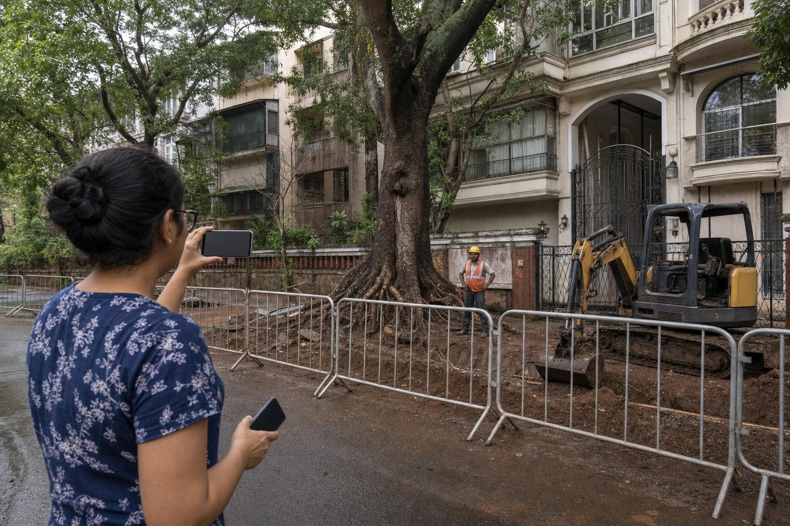A person records a wide view of a Mumbai tree, exposed roots and construction equipment from outside a barricaded work zone.