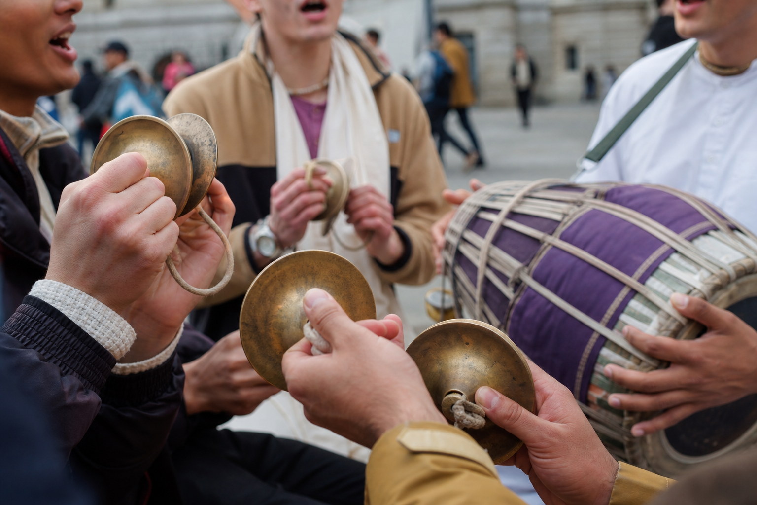 Hands play brass cymbals and a double-headed drum during a group chant on a London street.