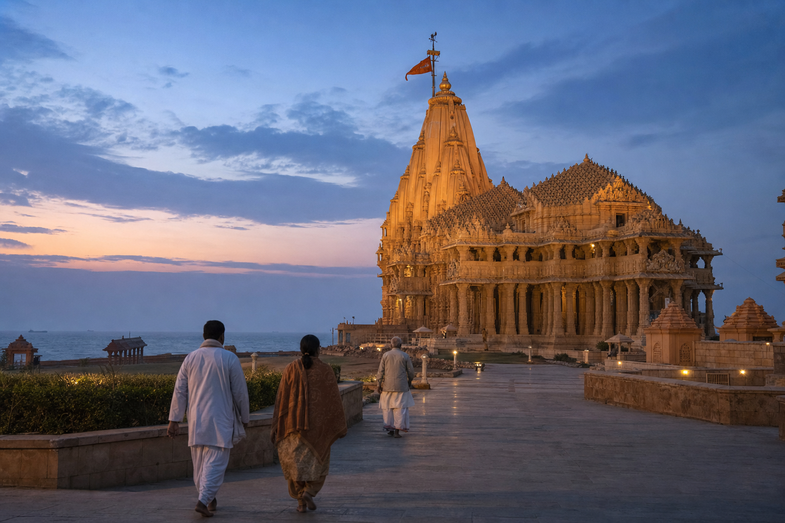 Pilgrims approach the illuminated sandstone Somnath temple near the Arabian Sea in the quiet light of early evening.