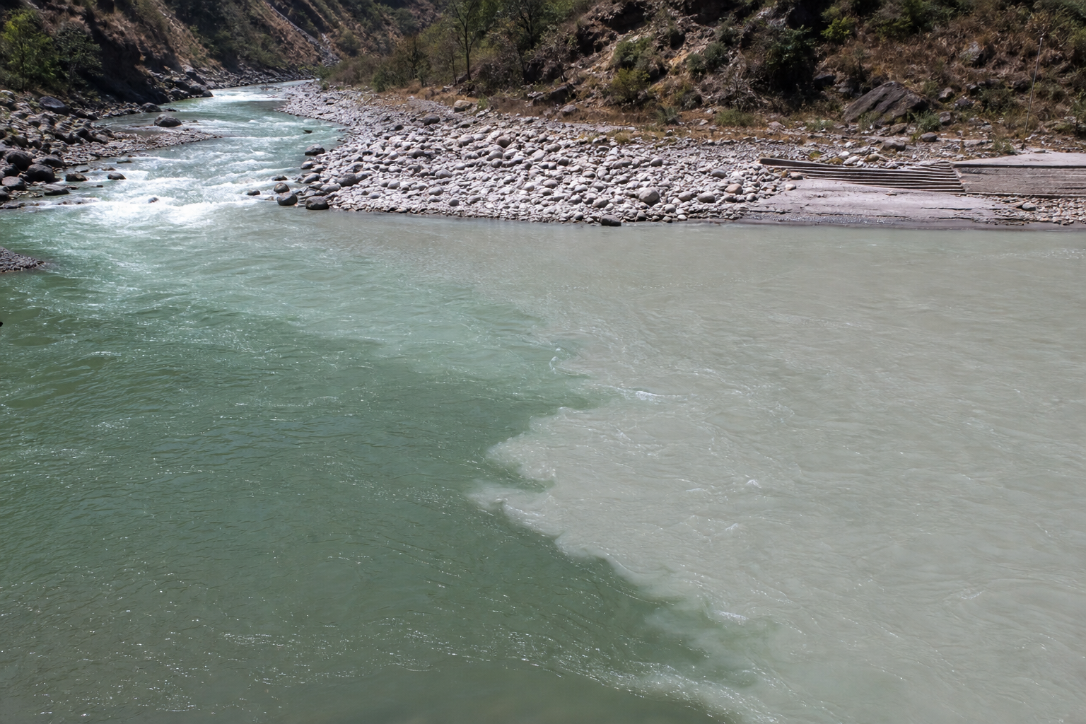 The narrower Nandakini River joining the wider Alaknanda River, with separate currents visible at the confluence.