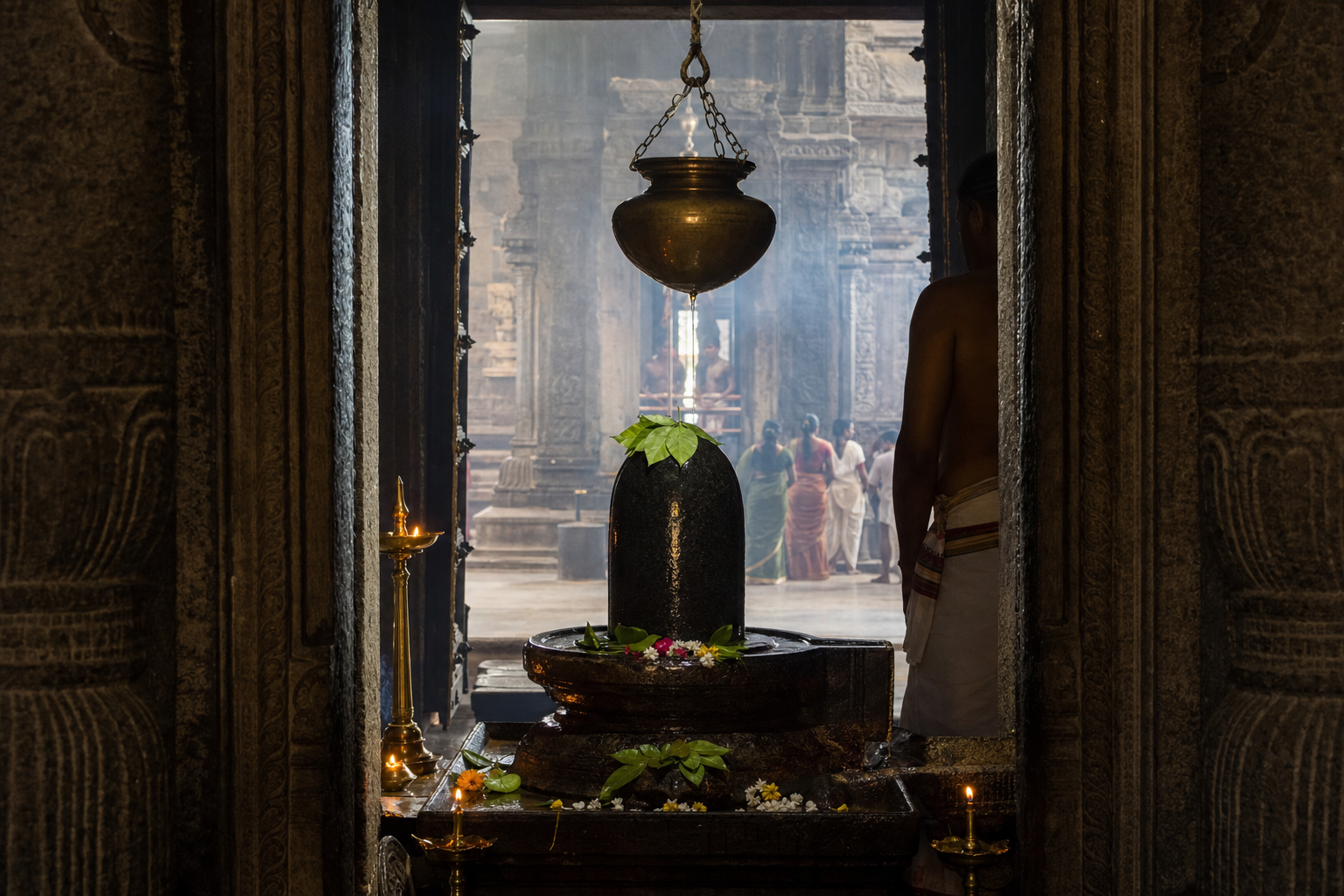 A stone Linga in a lamp-lit temple sanctum with ritual vessels, flower offerings, a priest and devotees visible through the carved doorway.