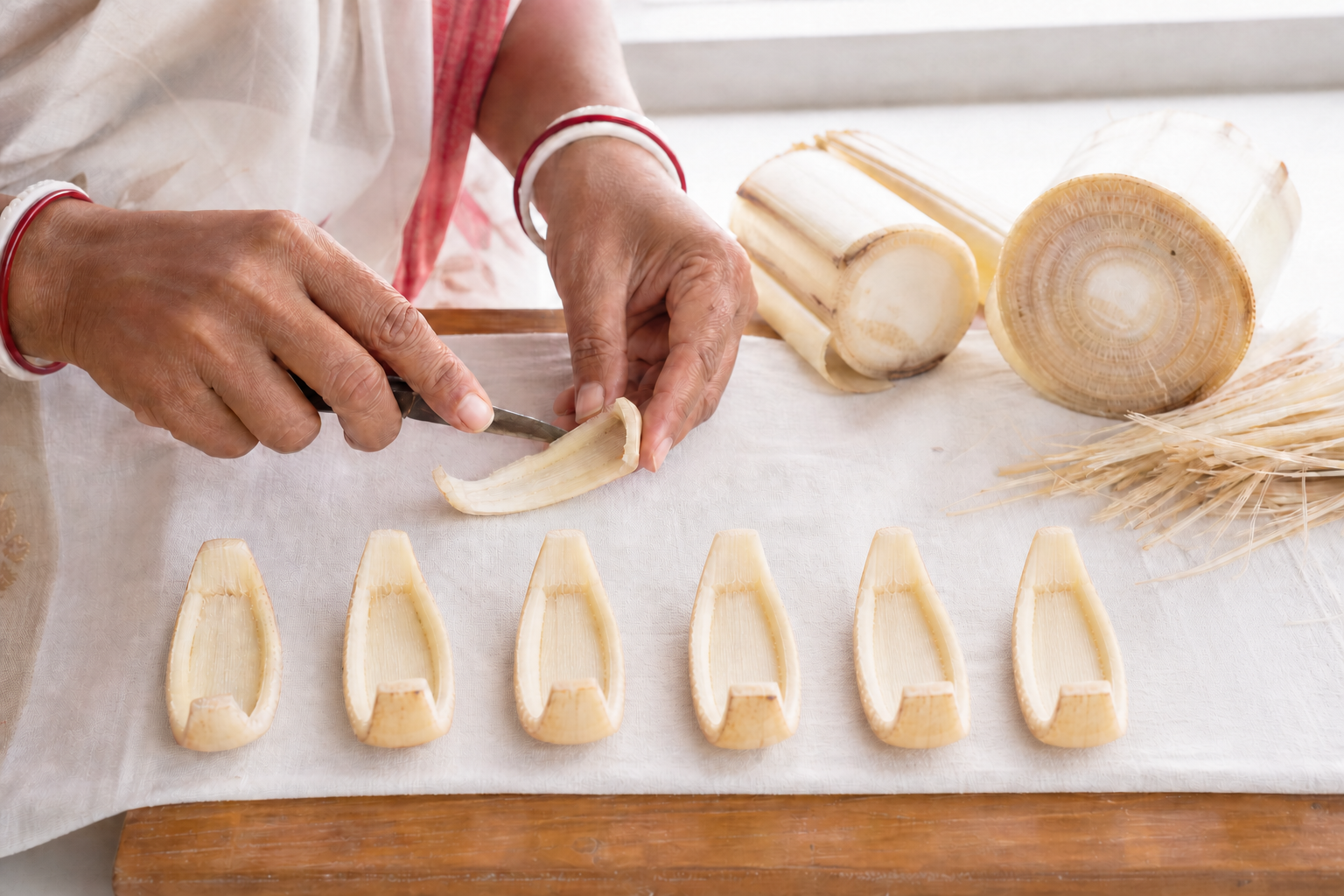Hands shaping banana pseudostem while seven small ritual boats are checked for stable, upright bases.