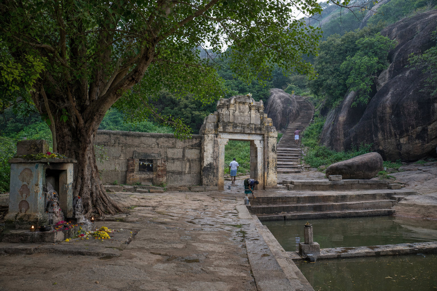 Pilgrims pause beside a gateway, sacred tree, small shrine, and stepped water tank at the foot of a South Indian temple hill.