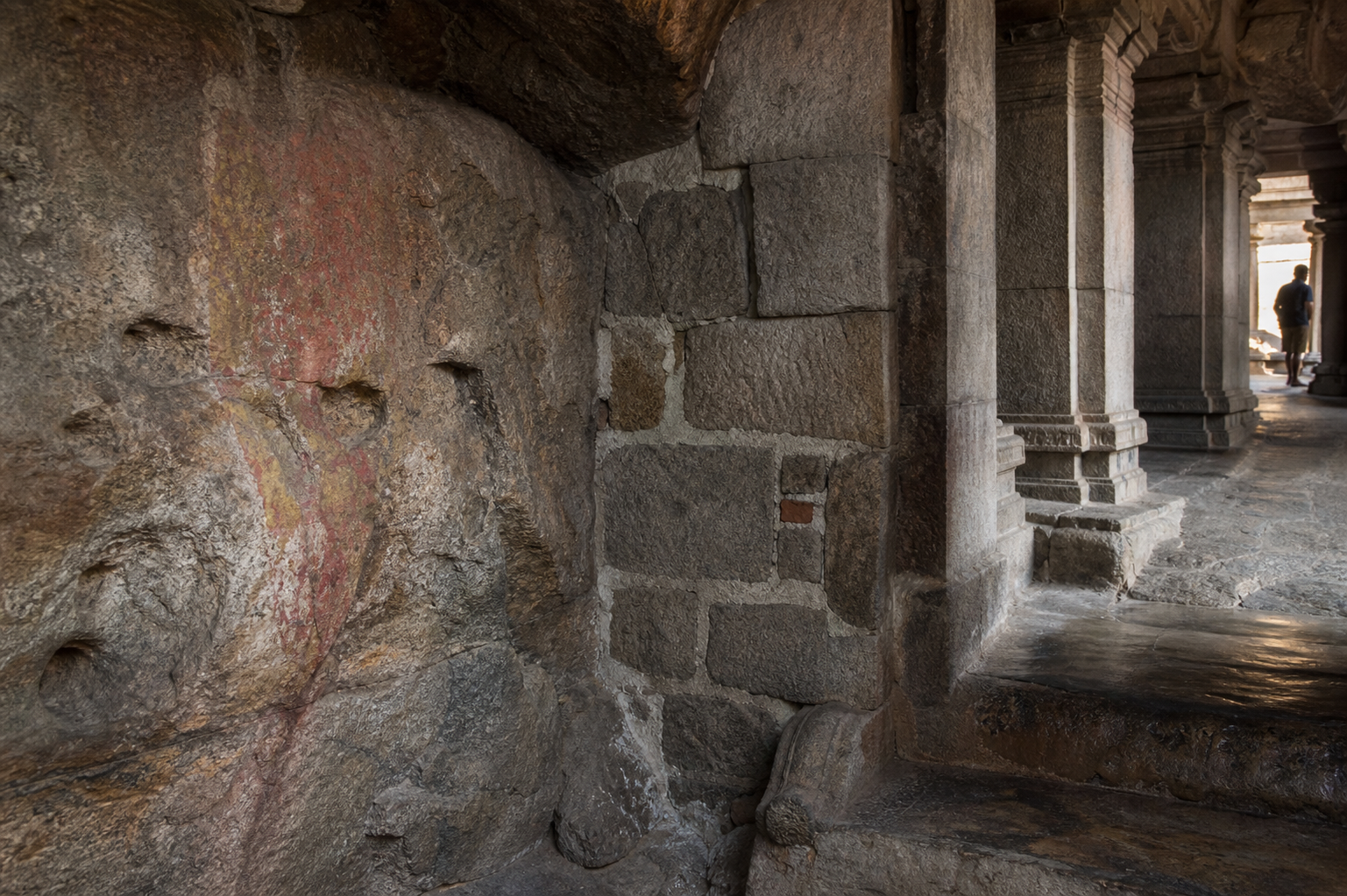 Weathered rock-cut surfaces, granite columns, repaired masonry, and a worn threshold reveal several construction and conservation layers in a hill shrine.