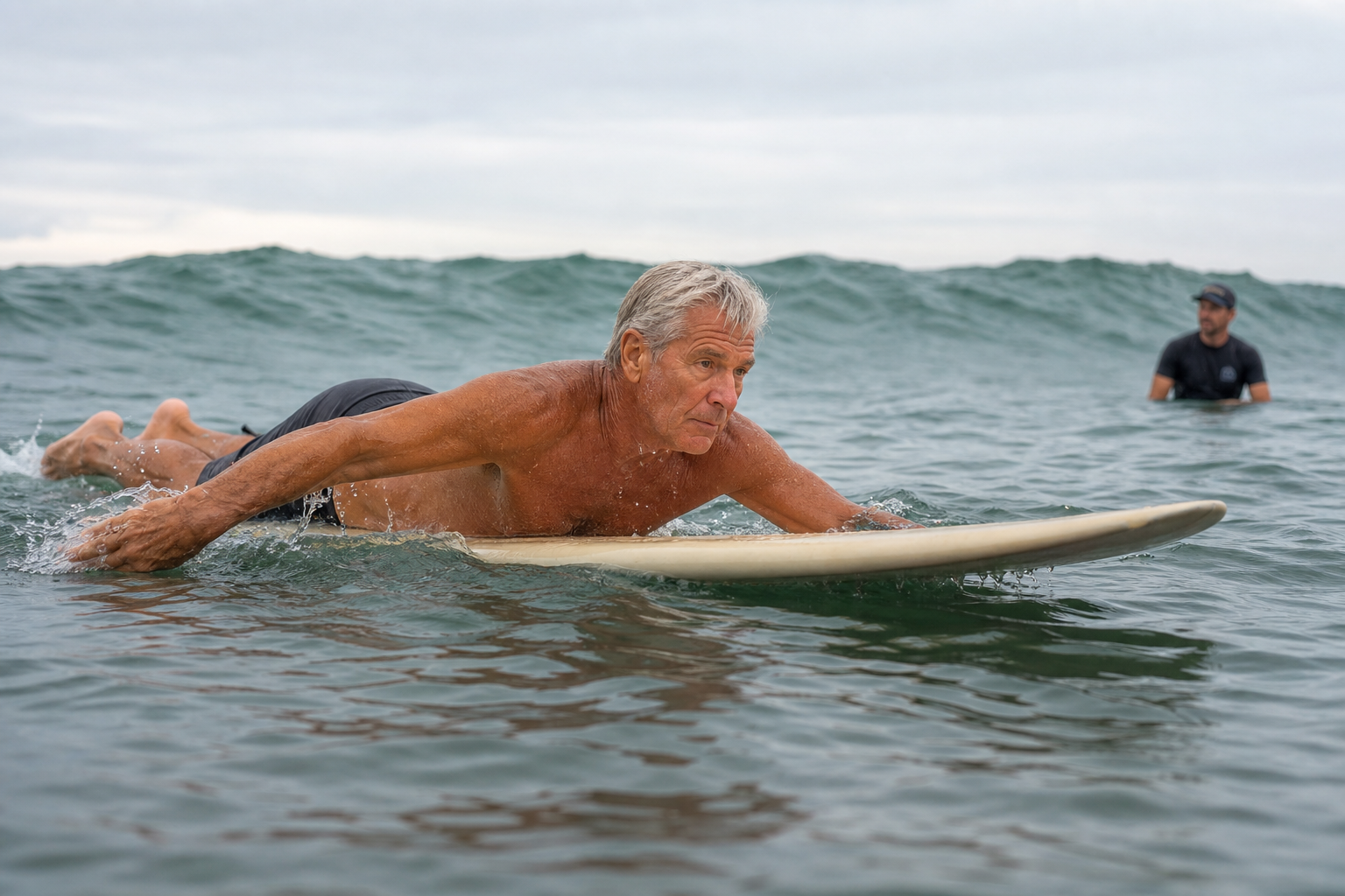 An older man practices balanced paddling on a longboard while a surf coach watches nearby.