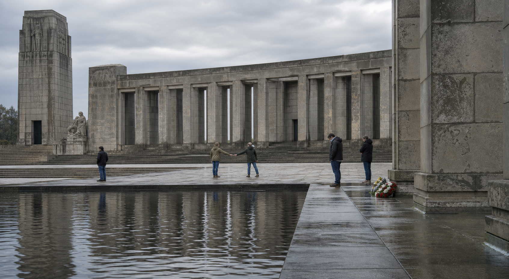 Two visitors pause in a posed movement at a war memorial plaza while other visitors stand quietly near floral tributes.