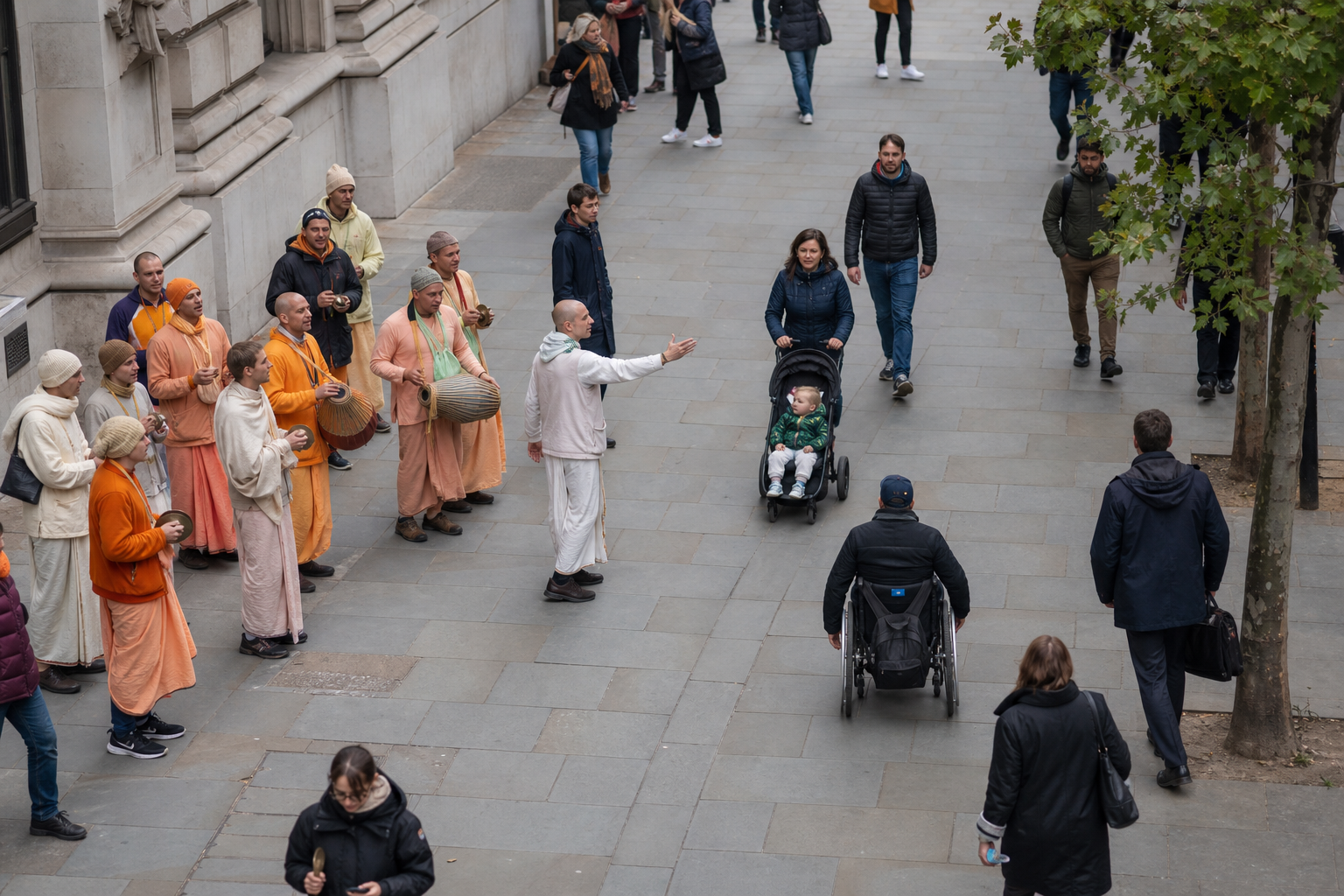 A Hare Krishna chanting group keeps to one side of a London pedestrian area, leaving an open route for wheelchair users, families, and other passersby.