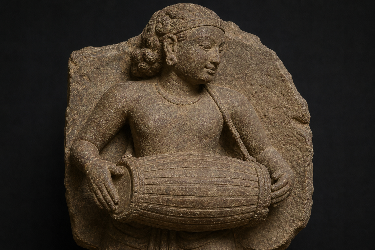 Detailed stone carving of a musician holding a long barrel-shaped drum with two visible heads and hands at opposite ends.
