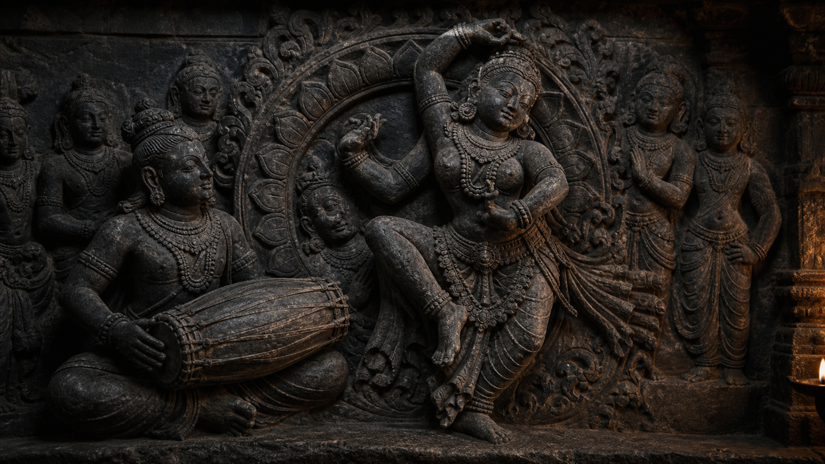 Dark stone relief of a drummer and sacred dancer linked by repeated curved gestures, ornaments, and lotus motifs.