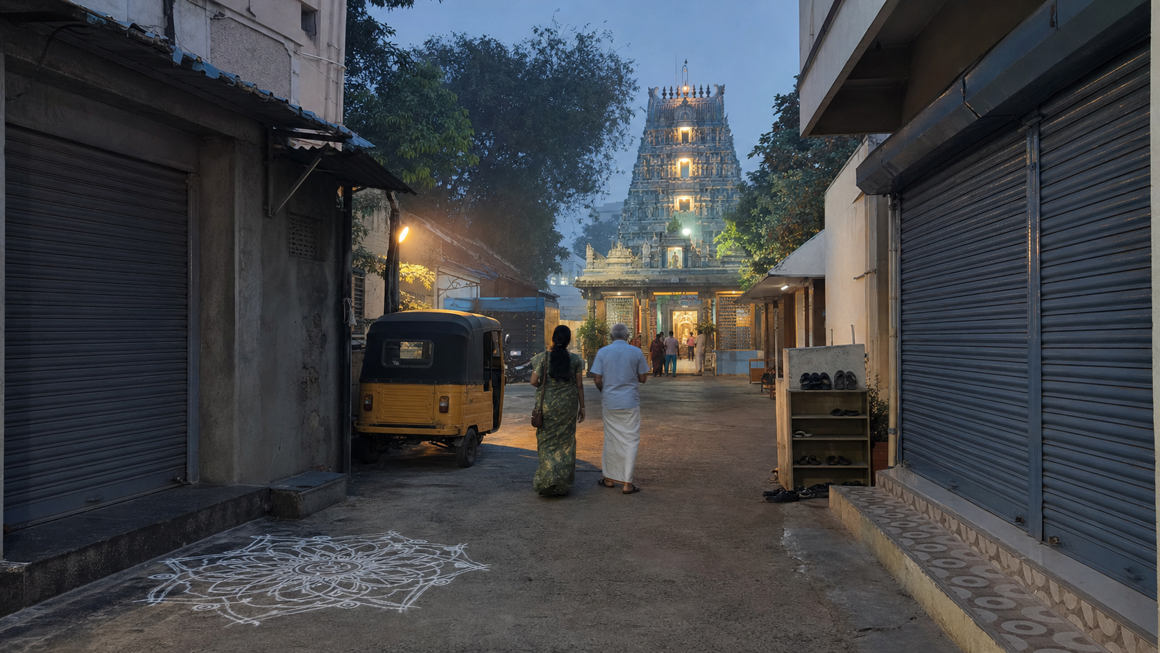 Two devotees walk along a quiet Chennai lane toward a temple before sunrise, with a kolam, an auto-rickshaw, and the illuminated gopuram ahead.