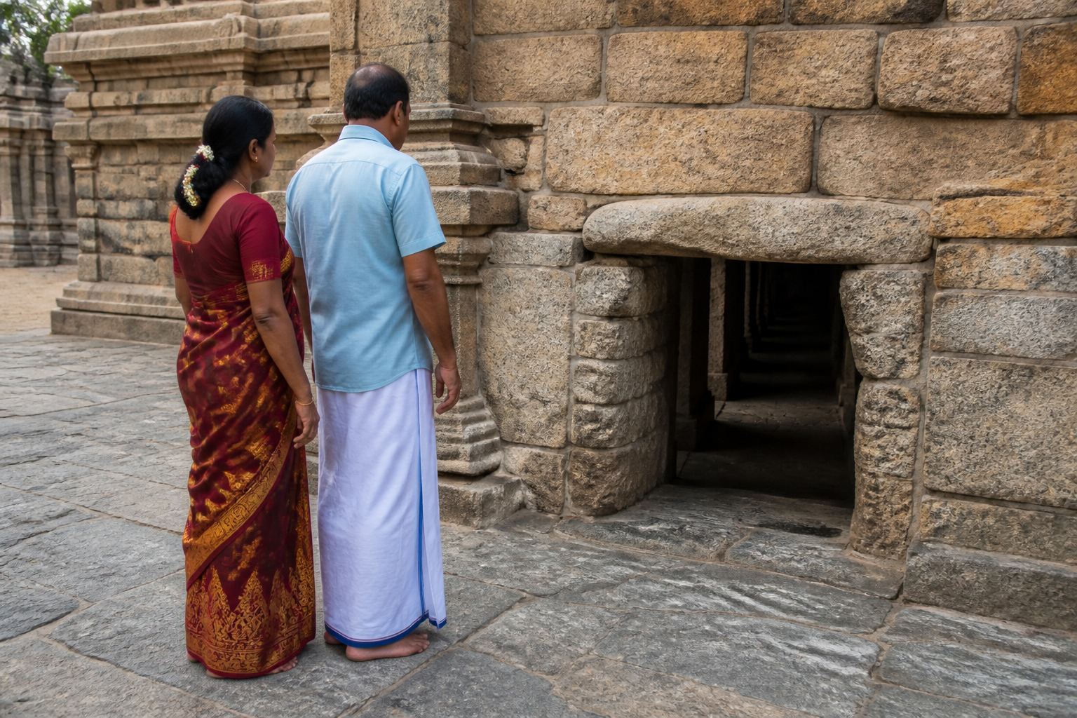 Two pilgrims pause in the open area to assess an empty, low and narrow stone passage before deciding whether to enter.