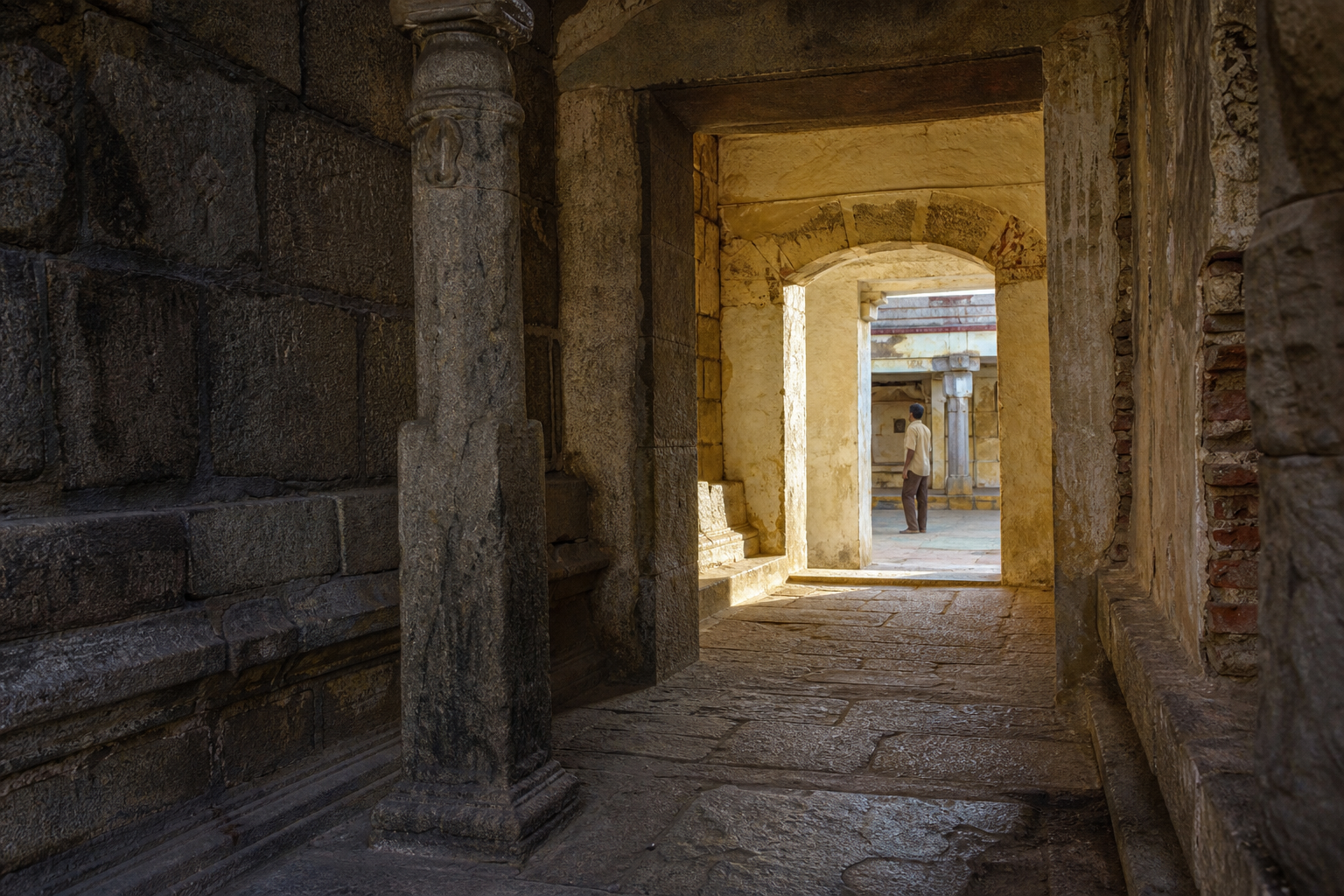 A weathered temple corridor with stonework, masonry, and plaster repairs from different building periods.