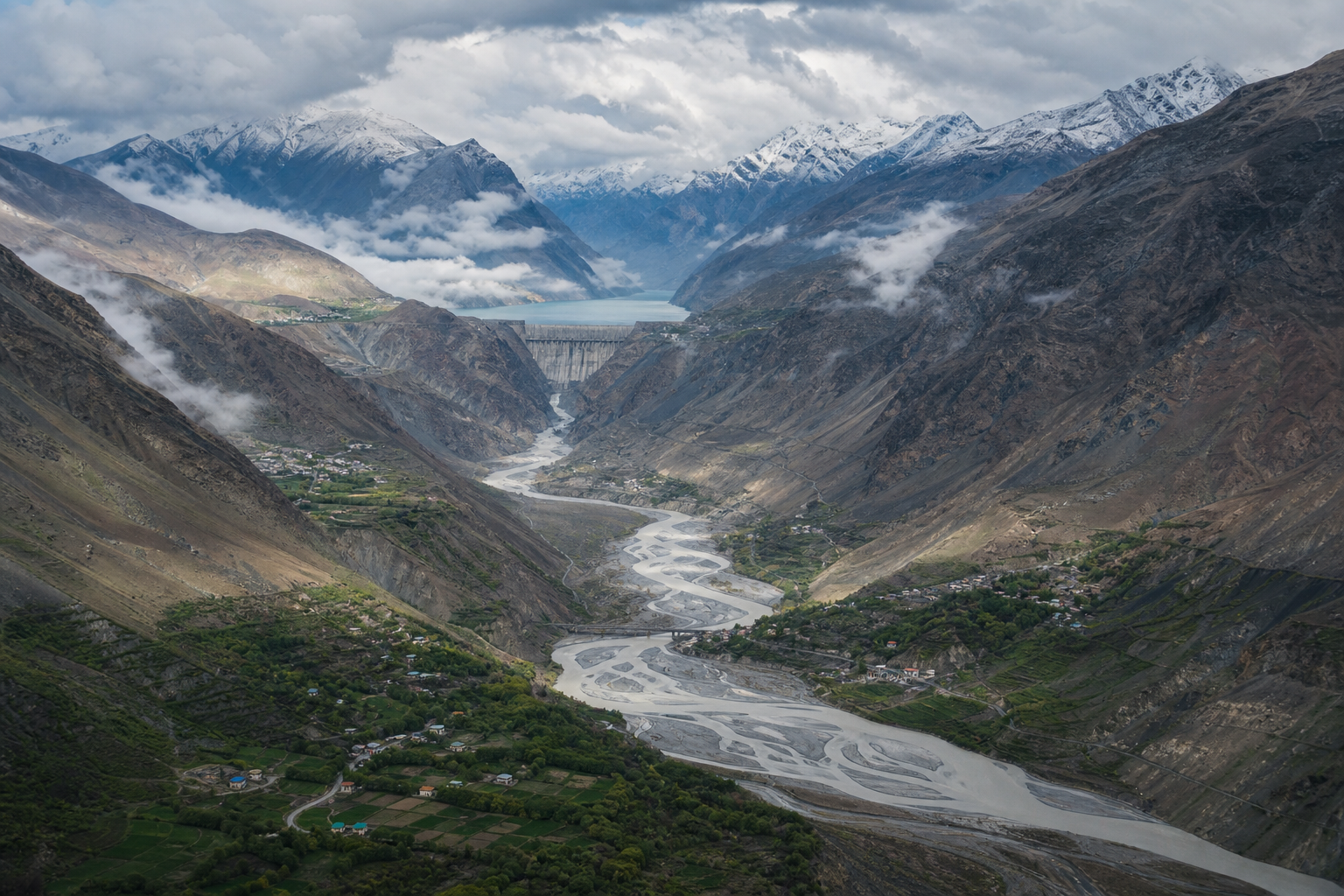 A large hydroelectric dam in a high Himalayan gorge above a river flowing toward green foothills, farms and downstream settlements.