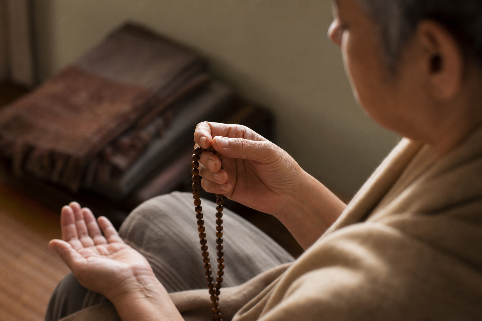 A practitioner's hand advances one wooden japa bead while the person refocuses in a quiet meditation corner.