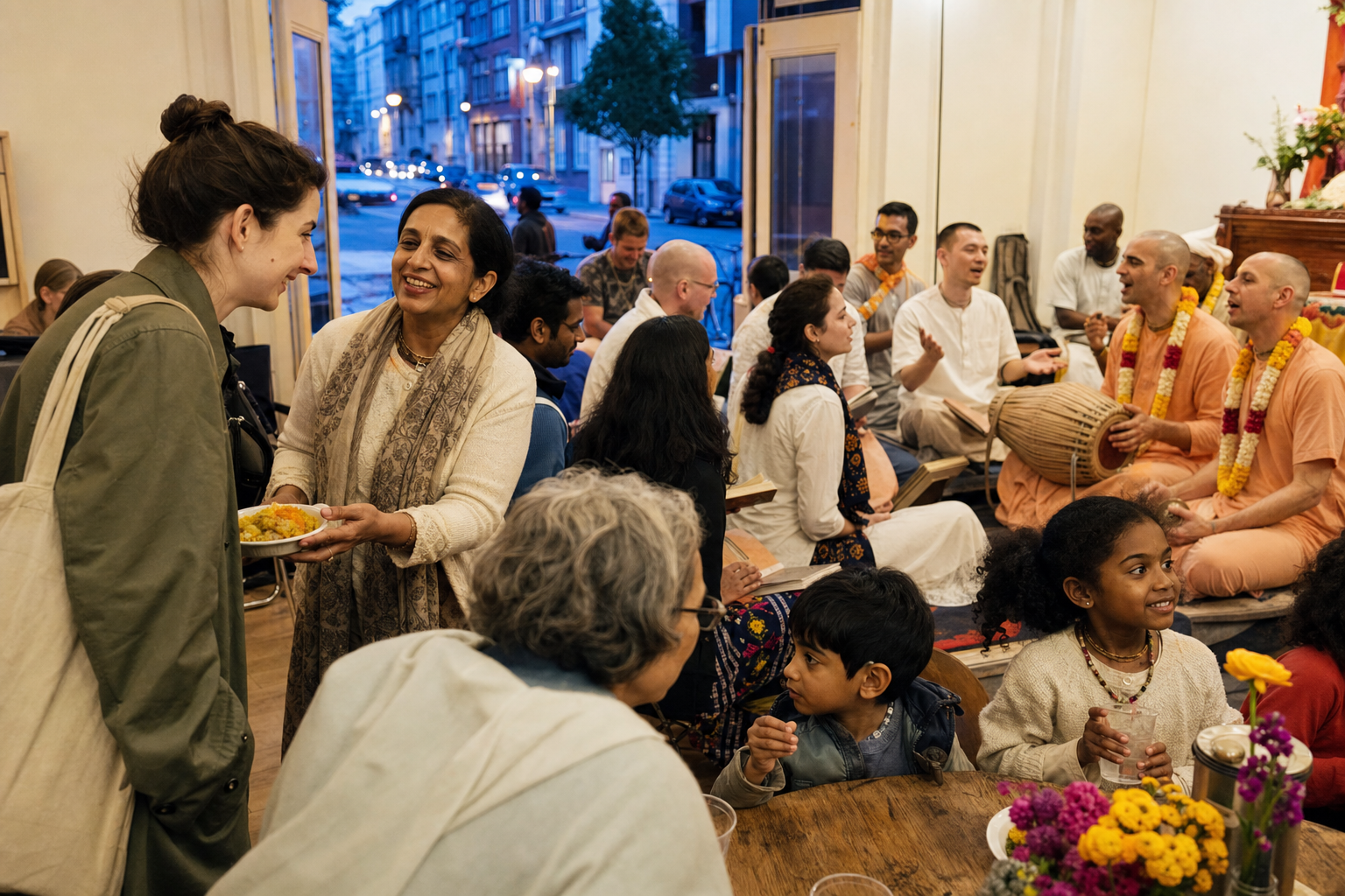 A newcomer receives vegetarian prasada at a community hall where people also share a meal, discuss devotional teachings, and participate in kirtan.