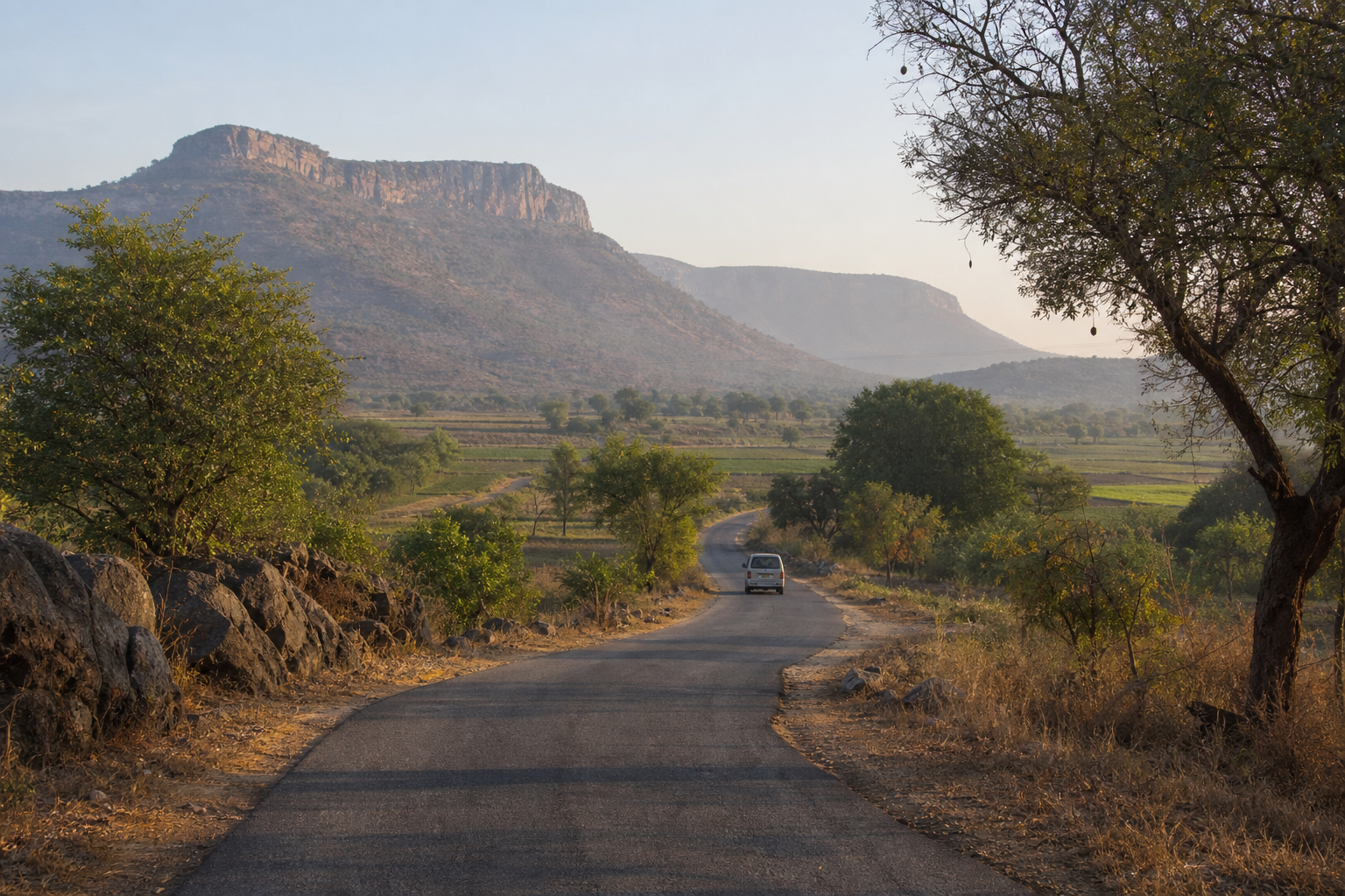 A vehicle follows a winding rural road through dry fields and low hills in Andhra Pradesh.