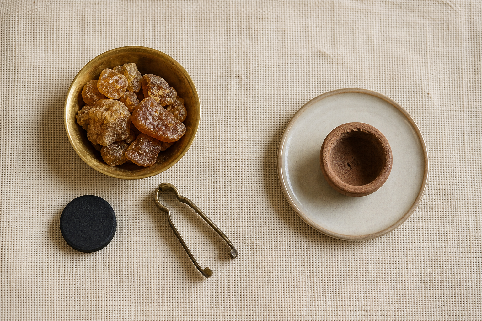 Loose brown sambrani resin with charcoal and tongs sits beside an unlit earthen dhoop cup on a ceramic saucer.