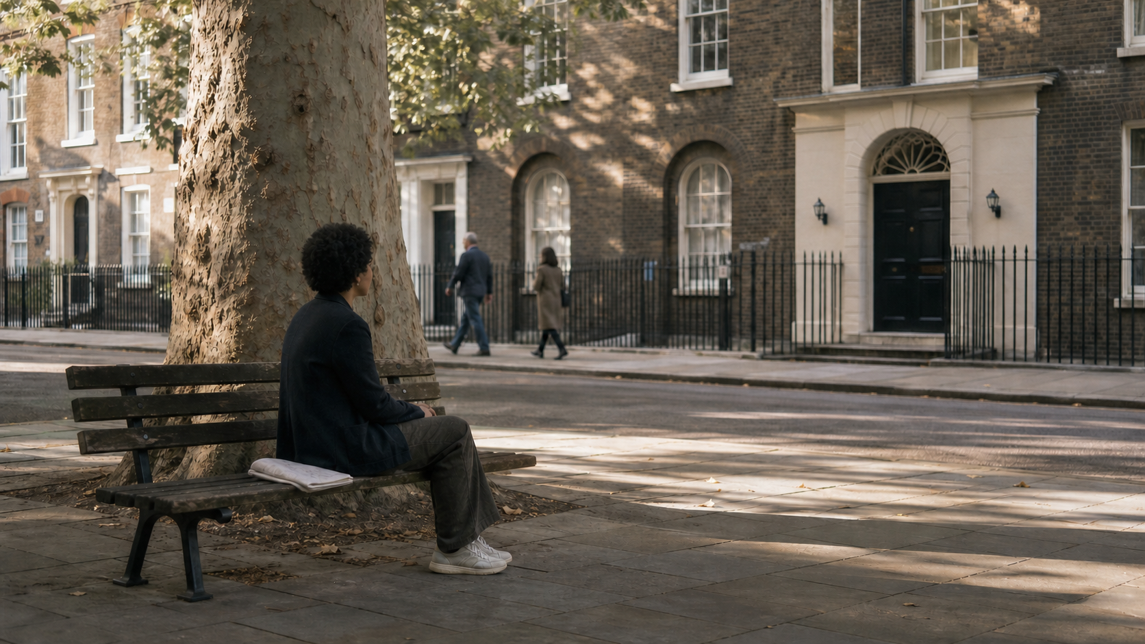 A visitor sits quietly on a public bench beneath a tree while facing a community doorway across a Bloomsbury pavement.