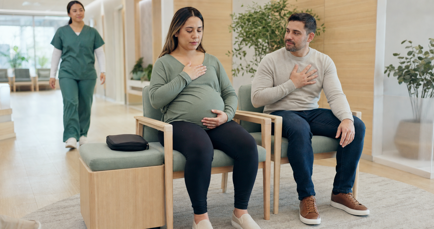 A pregnant woman practises a grounding breath in a clinic waiting area with a support person beside her and a nurse nearby.