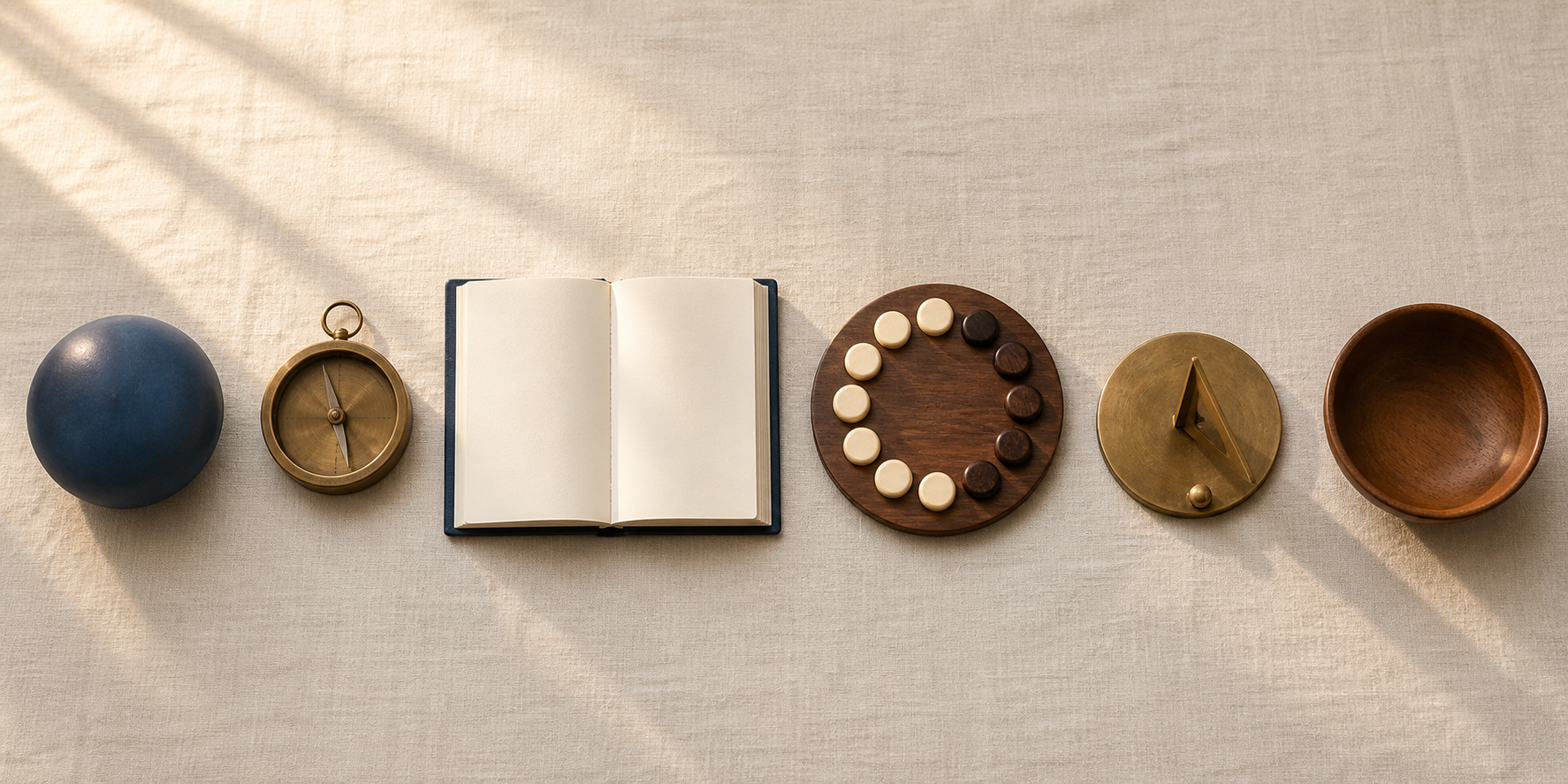 An overhead arrangement includes an unmarked globe, compass, blank almanac, lunar discs, sundial, and empty bowl on a linen-covered table.