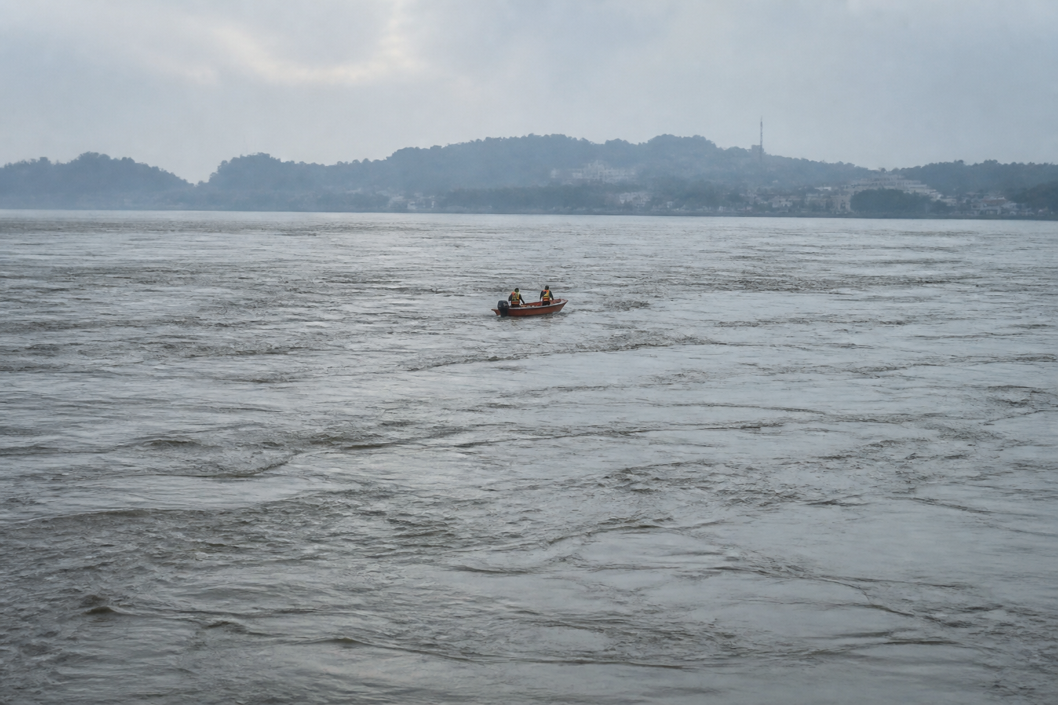 A search-and-rescue boat travels across the broad, fast-moving Brahmaputra River beneath an overcast sky in Guwahati.