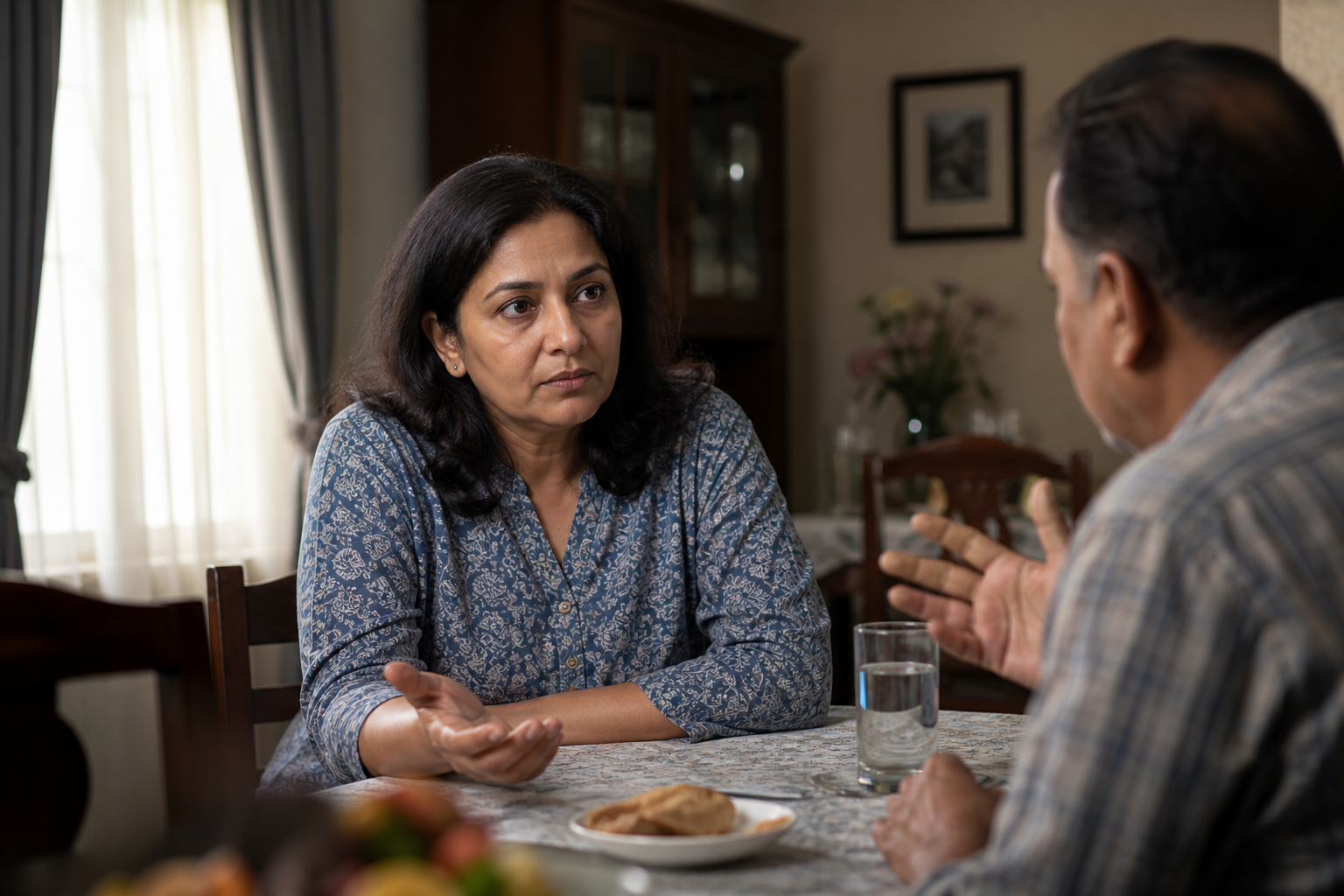 Two adults face each other during a tense family discussion while one pauses with a relaxed open hand before responding.