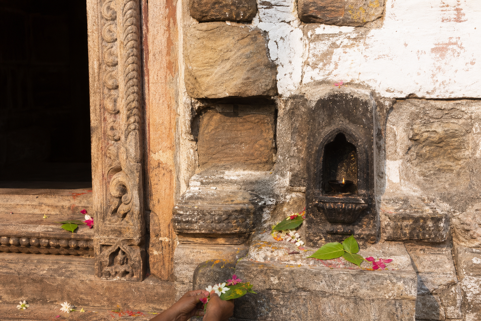 Weathered carvings, flower offerings, bilva leaves, and an oil-lamp niche mark an exterior doorway at Dhabaleswar Temple.