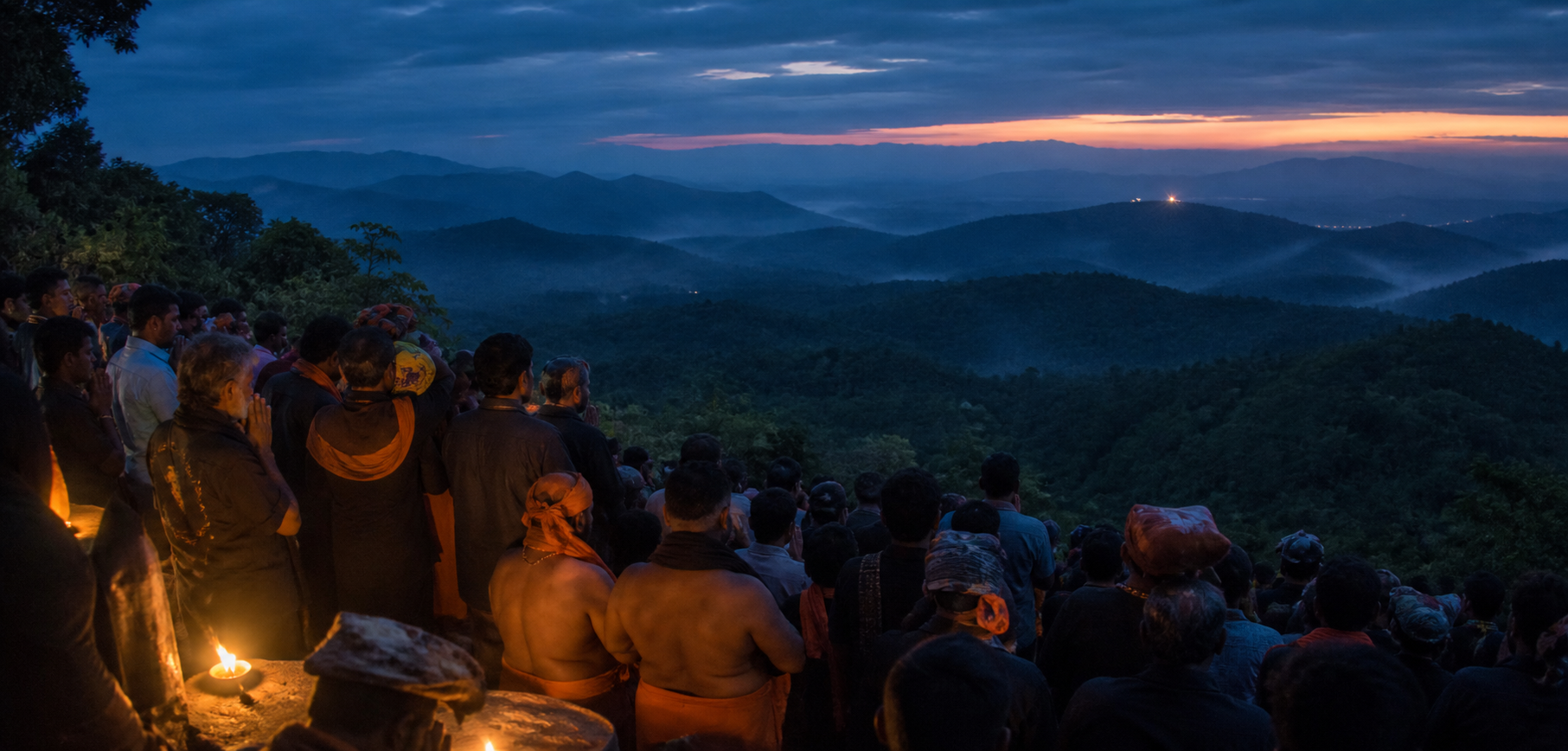 Pilgrims gather on a forested hillside at dusk and face a small distant glow during a Makarajyothi observance.