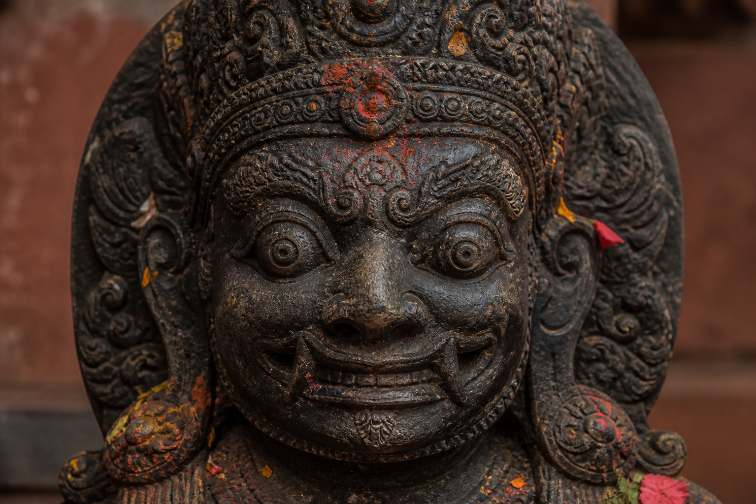 Close view of Kal Bhairav's dark stone face, with wide eyes, fierce features and a subtle smile beneath an ornate crown.