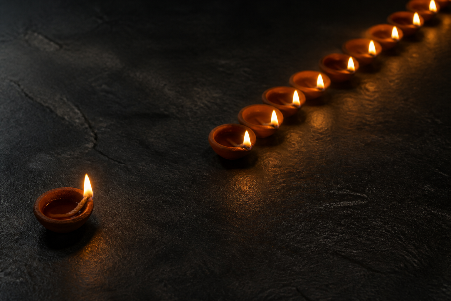A single clay diya sits apart from an ordered line of glowing diyas on a dark stone surface.