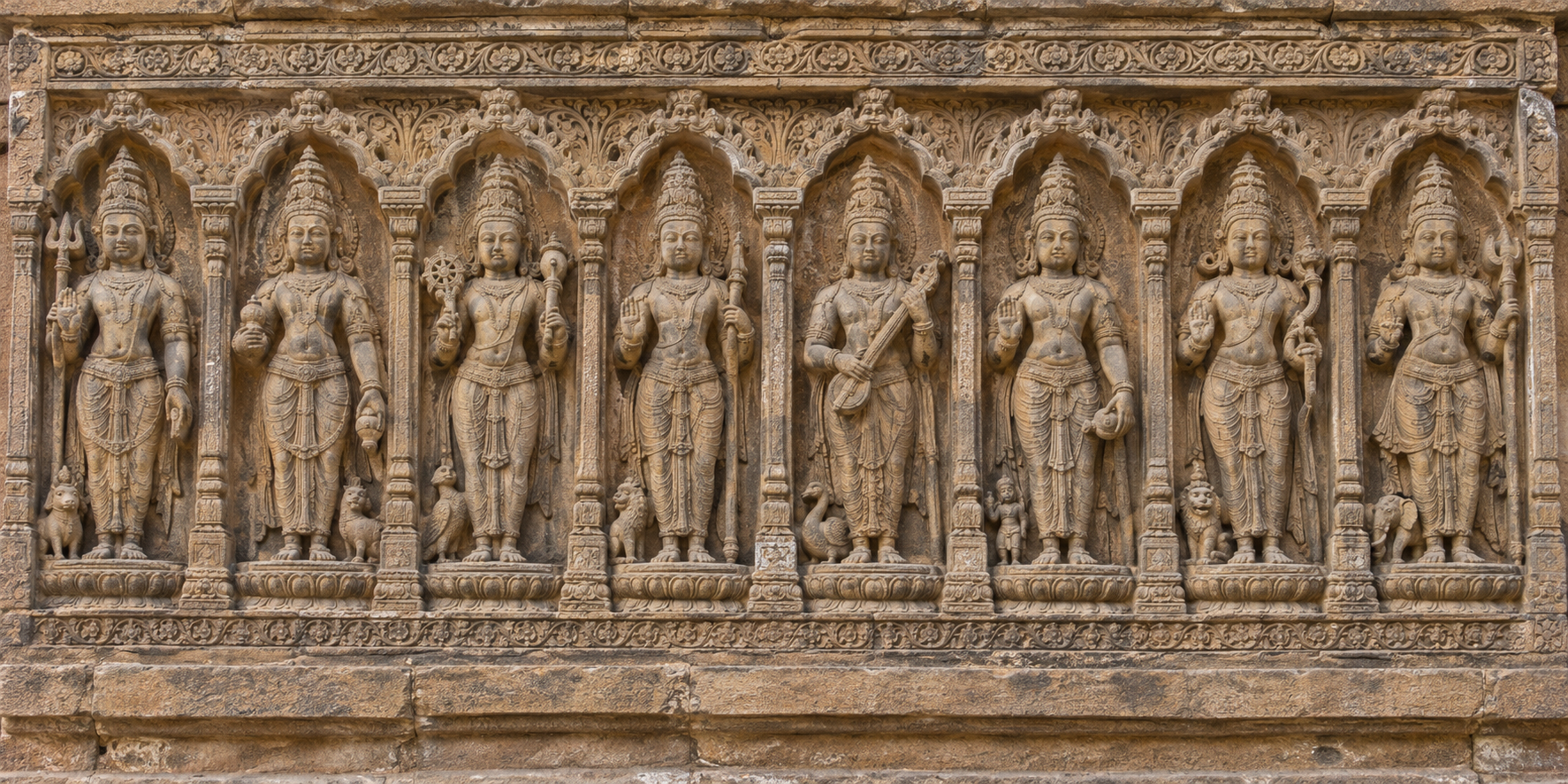 Eight standing deities occupy aligned sandstone niches joined by a continuous base and decorative border, showing that the carvings form a single ensemble.