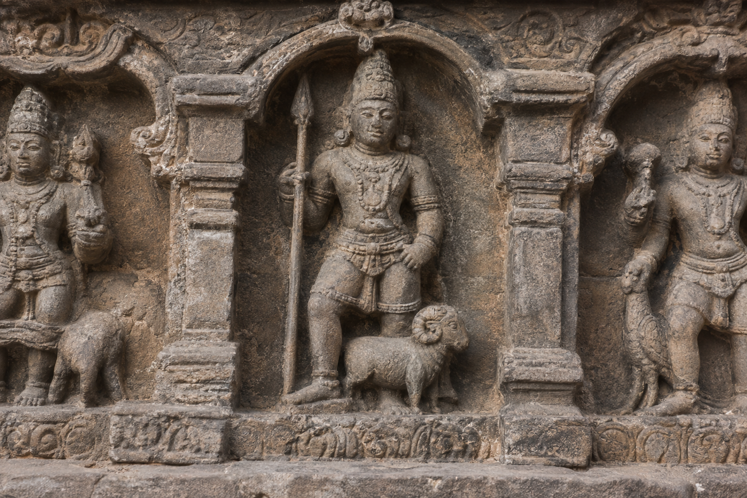Close view of a temple frieze with a spear-bearing male deity, a ram at his feet, and neighboring celestial figures at the edges.