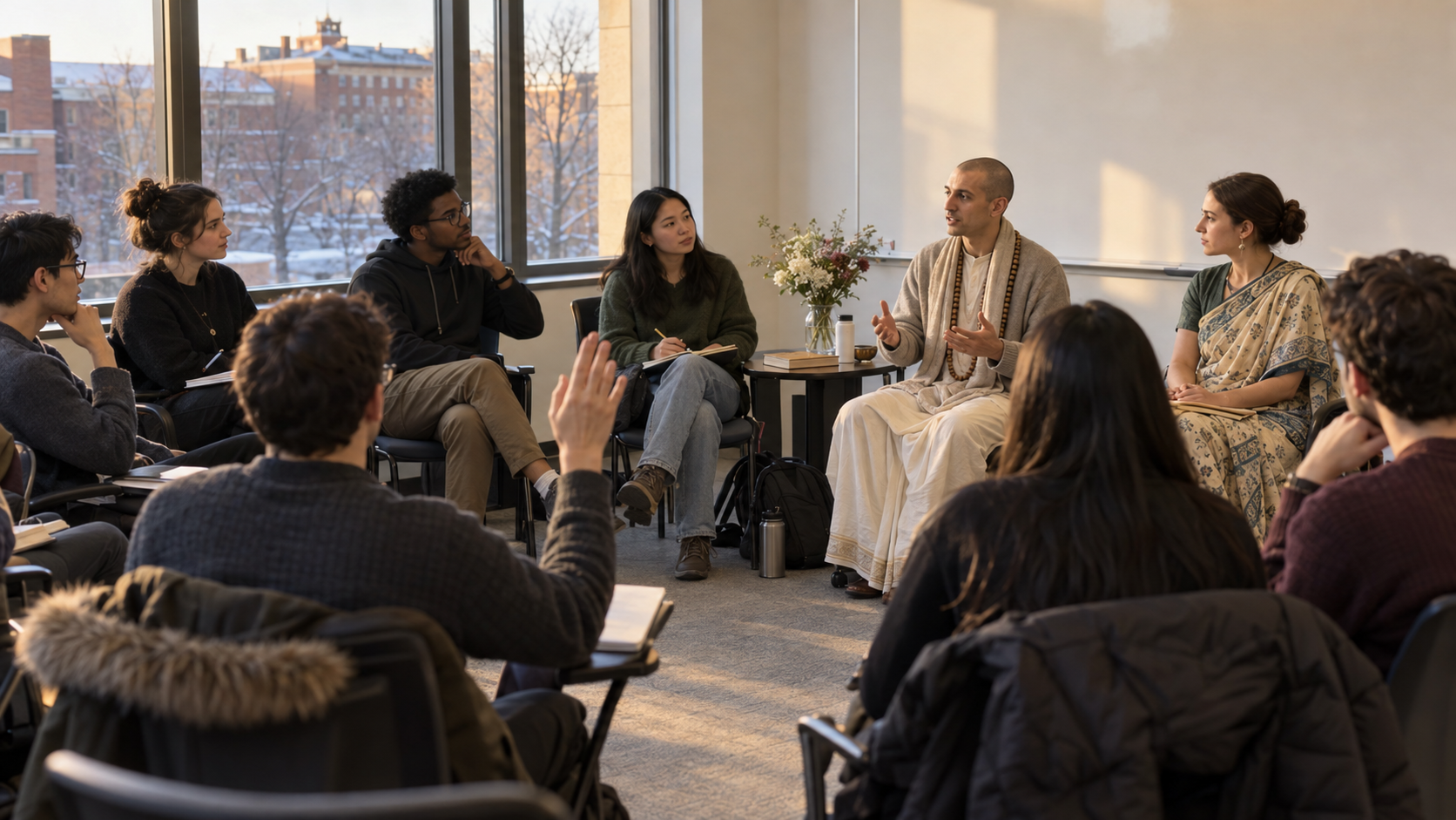 Students attend a small campus discussion led by two Vaishnava speakers in a university classroom overlooking red-brick buildings.