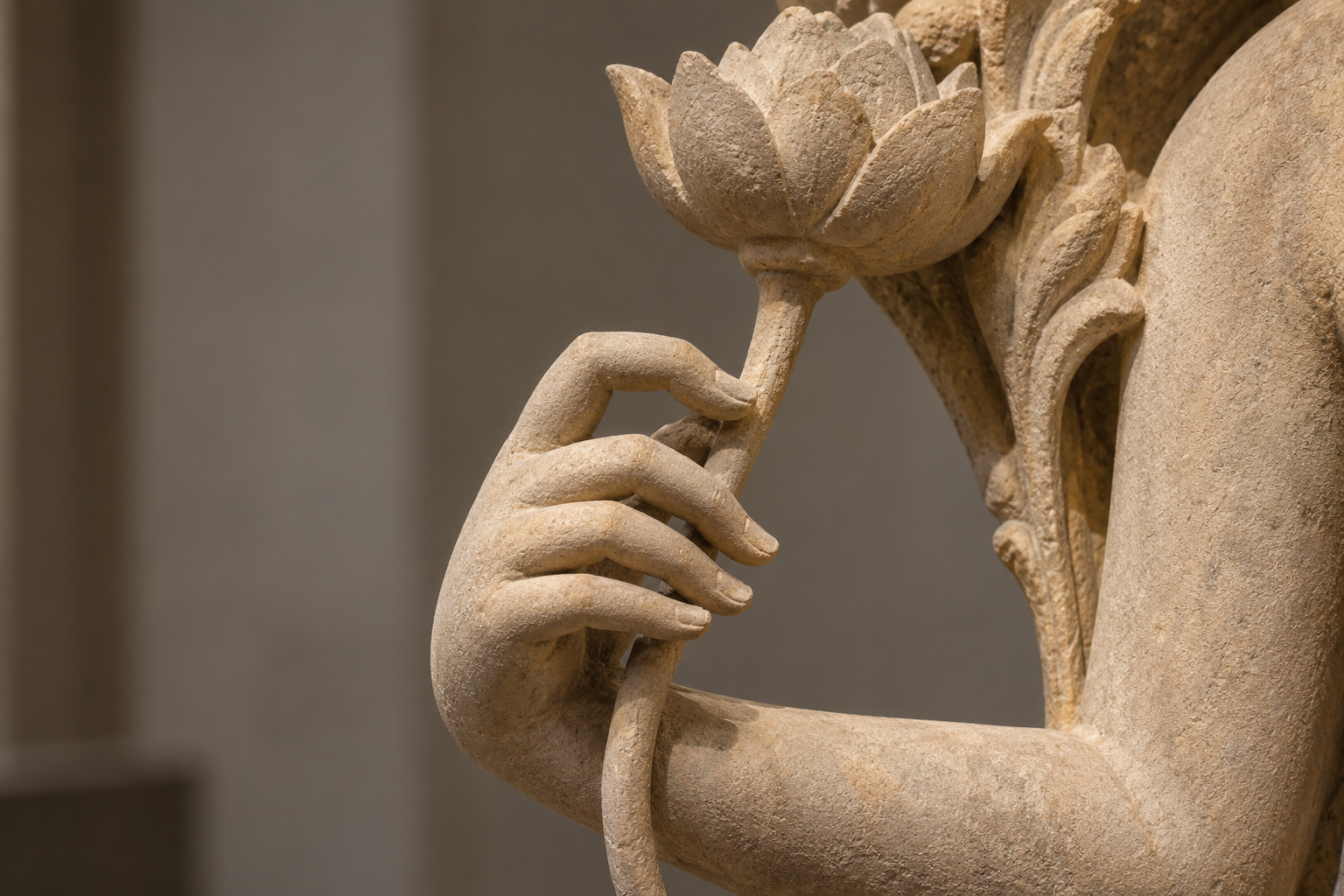 Carved stone hand forming a delicate grip around a lotus stem, with the blossom rising beside the figure's shoulder.