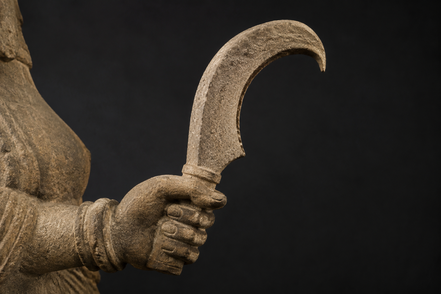 Side-profile close-up of a weathered sandstone hand holding a short crescent-shaped implement with an inner edge and hooked point.