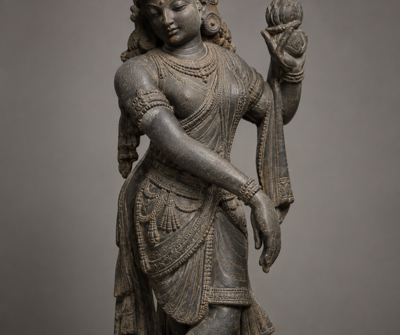 Close view of a stone dancing deity whose arm crosses the torso and ends in a relaxed downward-curving hand.
