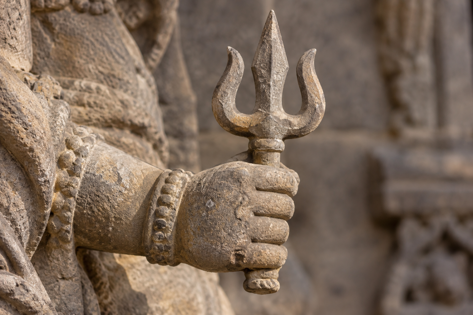 Close view of a weathered sandstone hand gripping a deliberately carved three-pronged object with a short shaft.