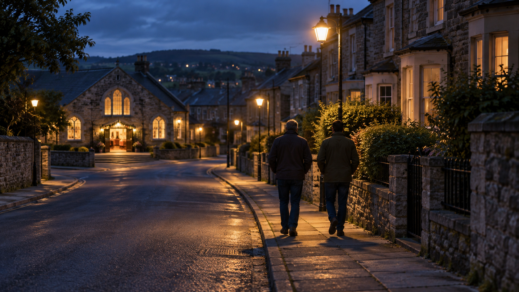 Two men walk along a dim residential street with a brightly lit community hall visible behind them.