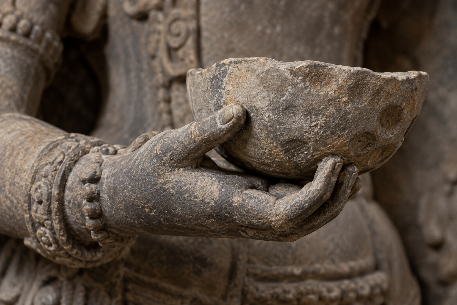 Close view of a weathered stone hand supporting a shallow bowl shaped from the rounded upper portion of a skull.