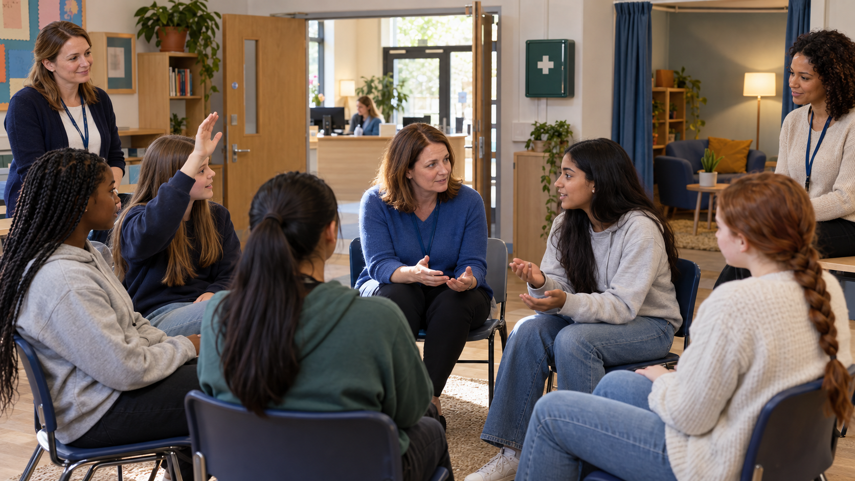 A safeguarding facilitator discusses an event setup with teenage girls in a classroom where adult volunteers and accessible support areas are visible.