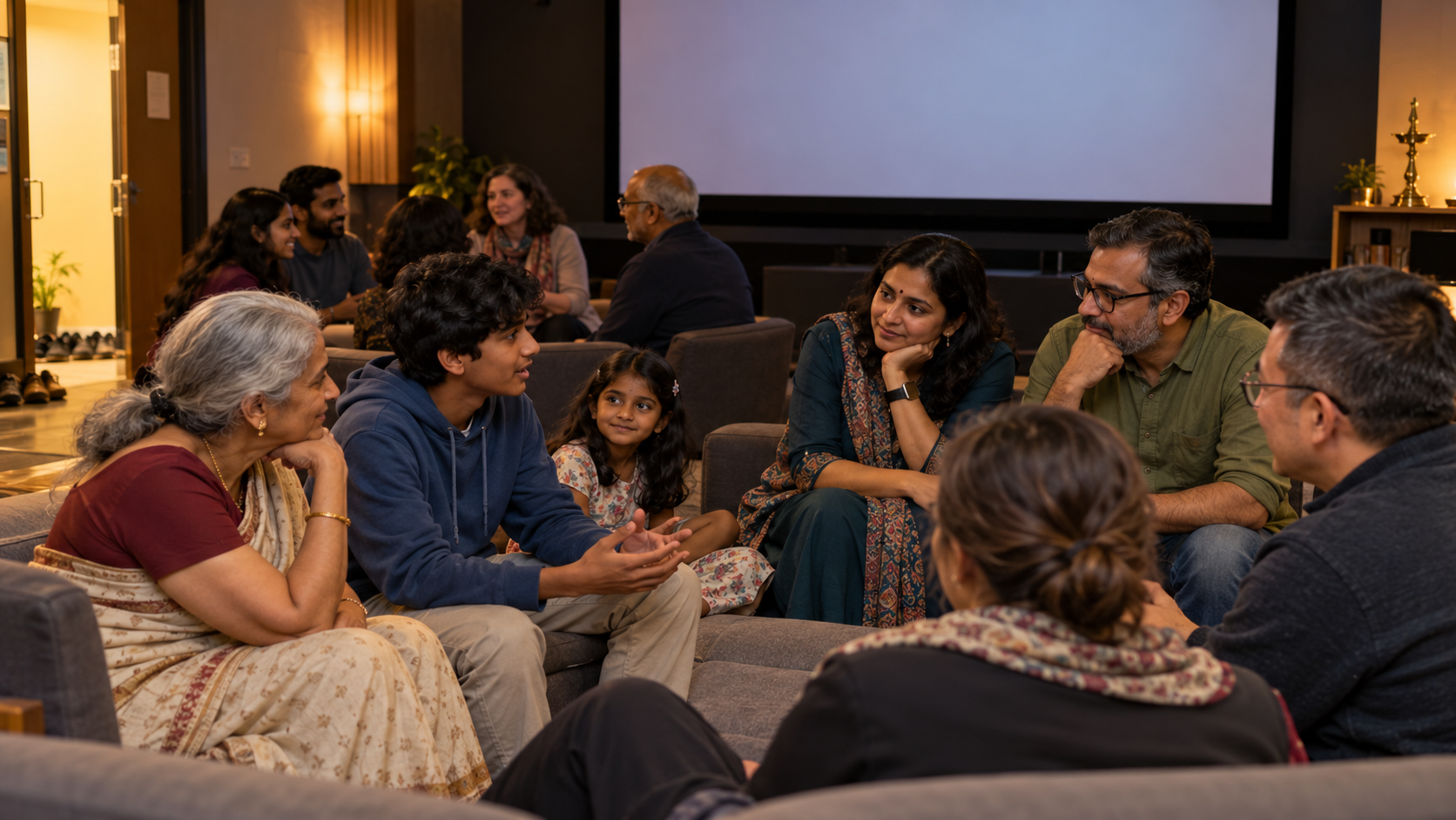 A multigenerational family and community group discuss a film together in a small screening room with a blank projection screen.