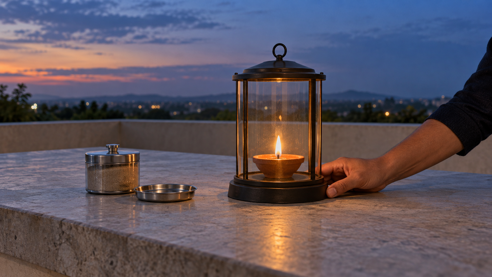 A supervised earthen lamp burns inside a glass-and-metal guard on a clear stone surface with a covered container of sand nearby.